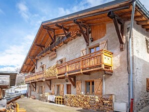 A traditional chalet with a wooden balcony, a stone facade, and a stack of firewood outside. - Chalet Honore by Interhome (Peisey-Nancroix)