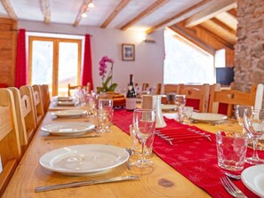 A dining table set with plates, cutlery, and glasses, with a red table runner and a bottle of wine. - Chalet Honore by Interhome (Peisey-Nancroix)