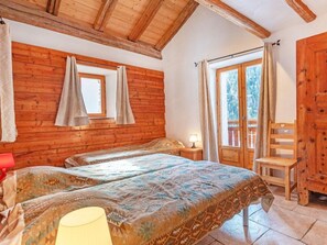 Quarto com paredes de madeira, cama com roupa de cama estampada, janela com cortinas e uma cadeira de madeira.