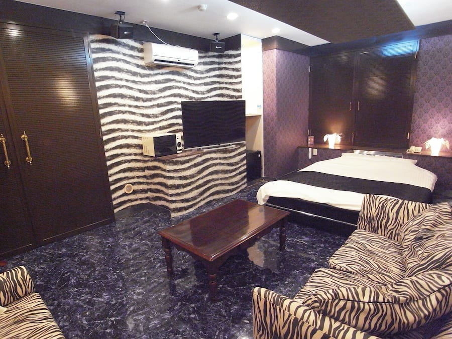 A hotel room with a bed, a sofa, a TV, and a wardrobe.