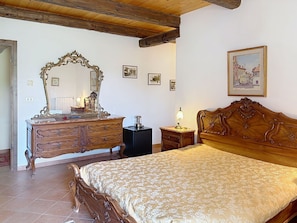 Ein Schlafzimmer mit einem Holzbett, einem Schminktisch mit Spiegel, einem Nachttisch mit Lampe und einem gerahmten Bild an der Wand.