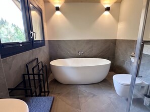 Ein modernes Badezimmer mit einer freistehenden Badewanne, einer Toilette und einem Fenster.