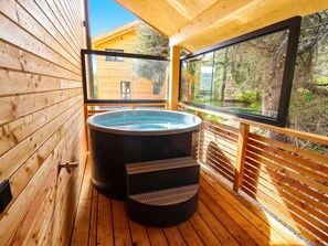 Eine Holzterrasse mit Whirlpool, Holzgeländern und Blick auf ein Holzgebäude.