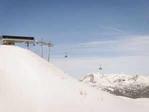 Eine Seilbahn mit Gondeln und Stahlseilen vor einer verschneiten Berglandschaft.