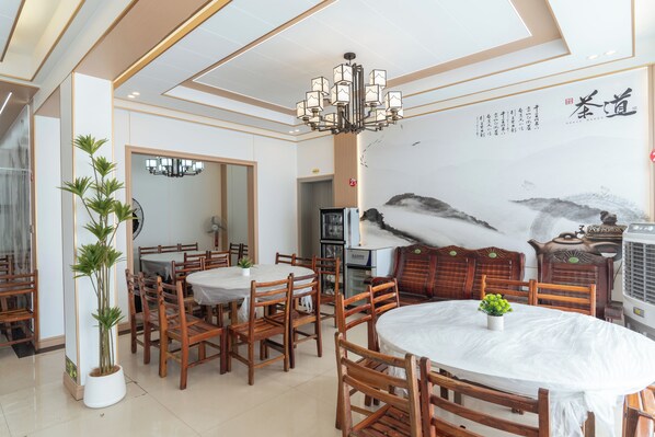 A dining area with wooden chairs and tables, a chandelier, and a wall with calligraphy.