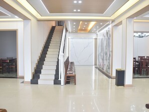 A spacious lobby with a central staircase, a marble wall, and a seating area.