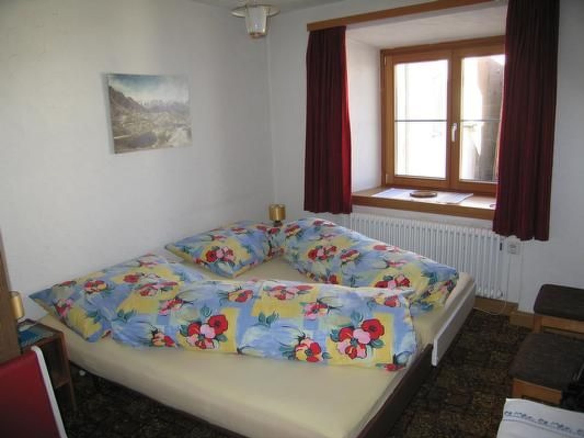 Une chambre à coucher avec un lit, une fenêtre avec des rideaux, un radiateur et un tableau accroché au mur.