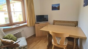 A room with a wooden table and chairs, a television on a stand, a window with curtains, and a picture on the wall. - Chasa Suzöl, (Lavin) by Interhome (Lavin)