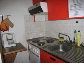A compact kitchen with a stove, sink, and a coffee maker.