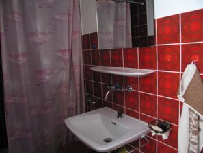 Um banheiro com pia branca, espelho, cortina de chuveiro e azulejos estampados vermelhos.