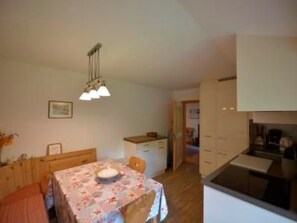 A small, cozy kitchen with a dining area. There is a table with a floral tablecloth and a hanging light fixture above it. - Via Paclera 23, (Sta. Maria - Santa Maria Val Müstair) by Interhome (Sta. Maria GR)