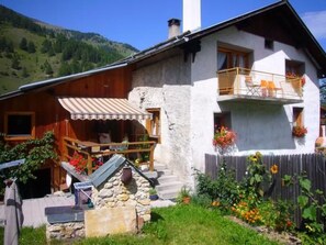 A two-story house with a stone facade, wooden balcony, and a small outdoor seating area. - Via Paclera 23, (Sta. Maria - Santa Maria Val Müstair) by Interhome (Sta. Maria GR)