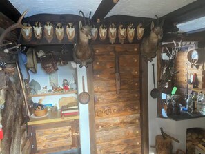 A rustic interior with wooden walls, a shelf with various items, and a ceiling with mounted animal skulls.