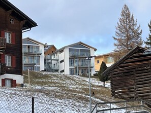 Ein modernes Gebäude mit großen Fenstern und einem Balkon, umgeben von verschneitem Gelände und Holzbauten.