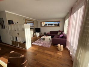 A living room with a purple sofa, a white coffee table, a TV, and a window with a view of a building. - Pellas, Vella, (Vella), 44014B by Interhome (Vella)