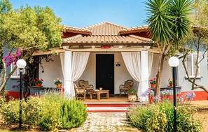 Un espacio de estar al aire libre techado con una mesa y sillas, rodeado de plantas en macetas y un sendero que lleva a una puerta.