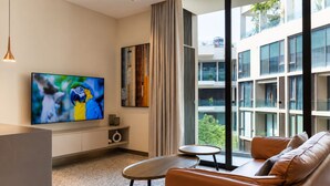 Una sala de estar moderna con una televisión de pantalla plana, un sofá, una mesa de centro y vistas a un edificio con balcones.