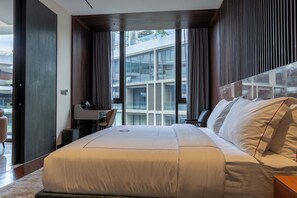 A modern hotel room with a large bed, a desk, and a view of a building through the window.