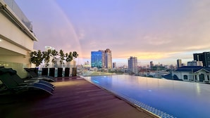 Una piscina infinita con vistas a un horizonte urbano, sillas de descanso y plantas en macetas.