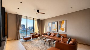 Una sala de estar moderna con un sofá grande, una mesa de centro y vistas a un paisaje urbano a través de ventanales de piso a techo.