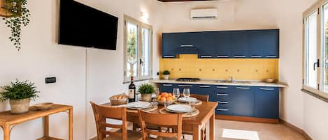 A modern kitchen with blue cabinets, a dining table with chairs, and a TV mounted on the wall.