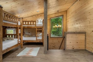 A cabin interior with bunk beds, a window with a view of trees, and a chandelier. - Views/HotTub/GameRoom/2FirePits/3Masters/Sleeps10! (Sevierville)