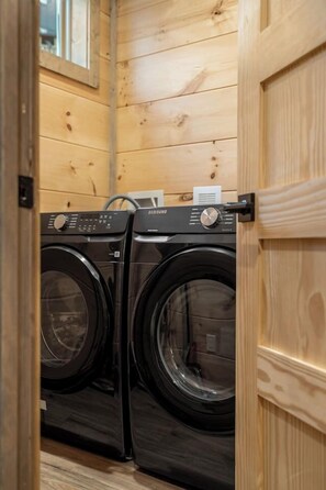 A laundry room with two black Samsung washing machines, wooden walls, and a door. - Views/HotTub/GameRoom/2FirePits/3Masters/Sleeps10! (Sevierville)