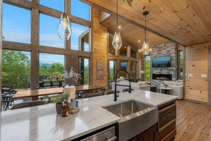 A spacious kitchen with a large island, wooden beams, and a stone fireplace. - Views/HotTub/GameRoom/2FirePits/3Masters/Sleeps10! (Sevierville)