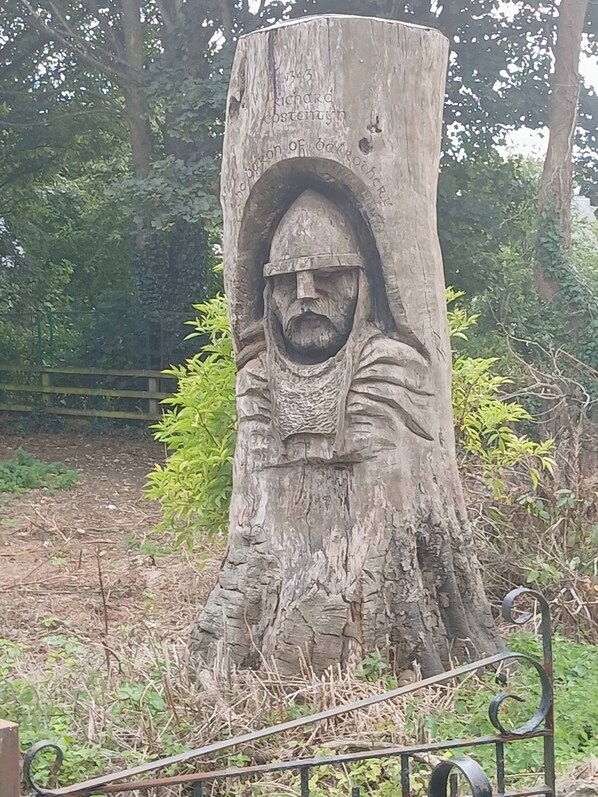 A tree with a carved figure, surrounded by greenery and a metal fence.