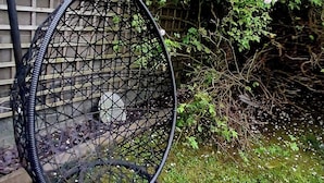Een tuin met een metalen stoel, een houten hek en begroeiing.