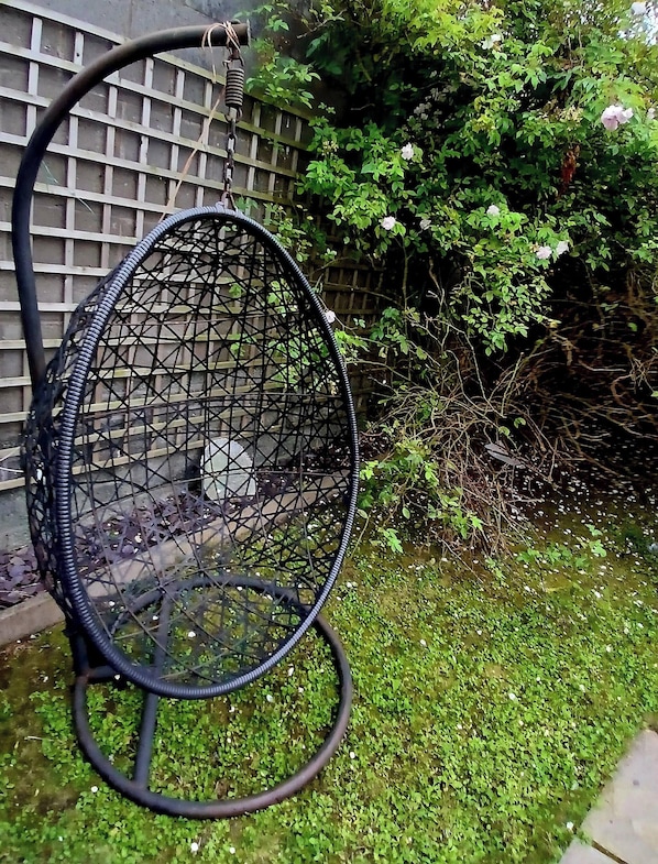 A garden with a metal chair, a wooden fence, and greenery.