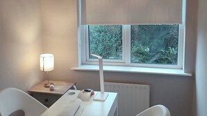 Een moderne kamer met een bureau, twee stoelen, een lamp en een raam met uitzicht op groen.