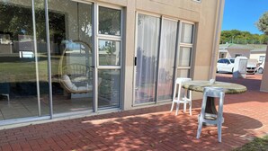 Eine Terrassenfläche mit Glastür, einem Korbstuhl und einem kleinen Tisch.