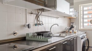 A modern kitchen with a built-in washing machine, stainless steel appliances, and a window with blinds. - Room-singh Leite Holiday Home (Lisbon)