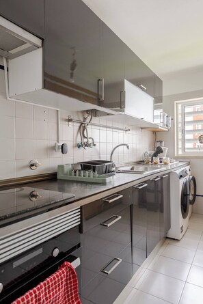 Una cocina moderna con lavadora integrada, electrodomésticos de acero inoxidable y una ventana con persianas.