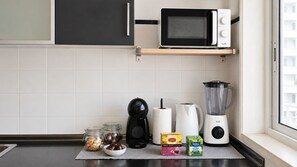 Una cocina con microondas, cafetera, licuadora y frascos de comida sobre la encimera.