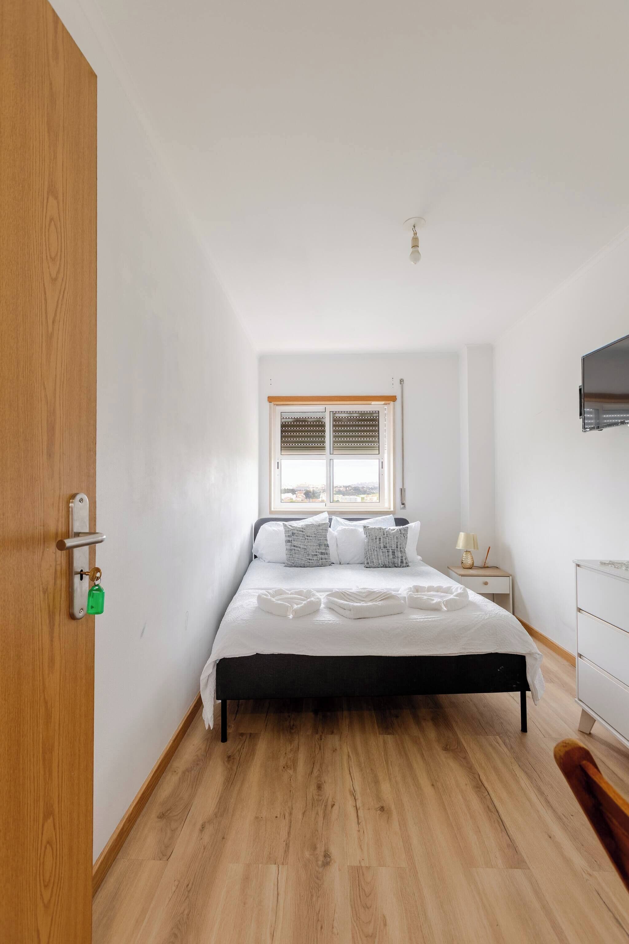 A bedroom with a bed, a nightstand, a TV, and a window with blinds.