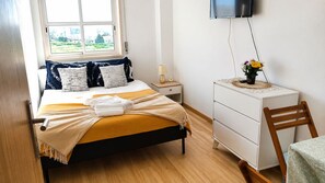 Un dormitorio con cama, mesita de noche, cómoda, silla y televisión en la pared.