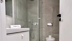 A modern bathroom with a glass shower enclosure, a white sink with a towel labeled "SuperHost," and a toilet with a trash bin beside it. - Le Bohémien Signature Apartment in La Marsa (La Marsa)