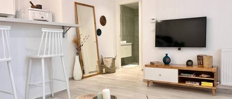 Ett modernt vardagsrum med en tv, vita barstolar, ett runt soffbord och en stor spegel.