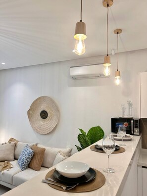 A modern kitchen with a central island, pendant lighting, an air conditioning unit, and a decorative wall hanging. - Le Bohémien Signature Apartment in La Marsa (La Marsa)