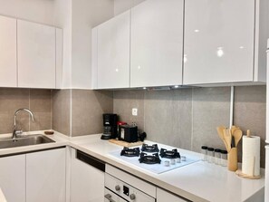 A modern kitchen with white cabinets, a stainless steel sink, a coffee maker, and a gas stove. - Le Bohémien Signature Apartment in La Marsa (La Marsa)