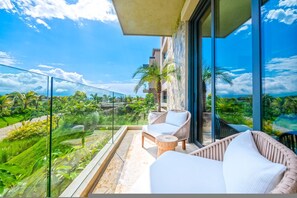 Ein Balkon mit Blick auf eine üppige Landschaft, ein Korbsessel und ein kleiner runder Tisch.