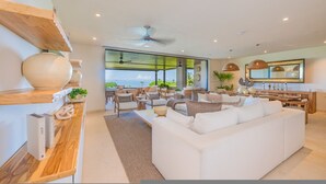 A modern living room with a white sofa, wooden shelves, and a view of the sea. - Condo Ensue o 3BD - Tau Punta Mita (Punta de Mita)