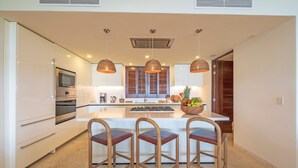 A modern kitchen with white cabinetry, a central island, wooden bar stools, and pendant lighting. - Condo Ensue o 3BD - Tau Punta Mita (Punta de Mita)