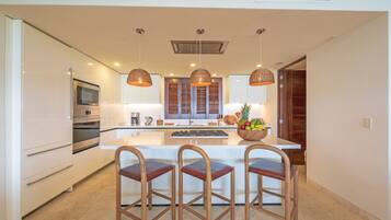 Una cocina moderna con armarios blancos, una isla central, taburetes de madera y luminarias colgantes.