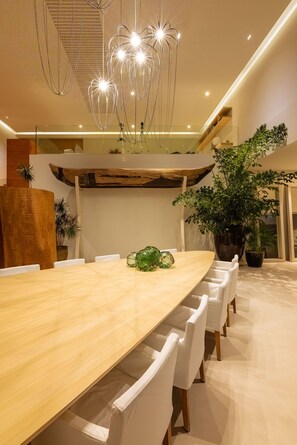 A modern dining area with a long wooden table, white chairs, and a unique chandelier. - Casa Brisa 7BD - Kupuri Punta Mita (Punta de Mita)