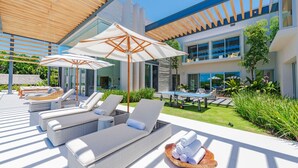 Een moderne buitenlounge met ligbedden, parasols en een pooltafel.