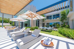 A modern outdoor lounge area with sun loungers, umbrellas, and a pool table. - Casa Brisa 7BD - Kupuri Punta Mita (Punta de Mita)