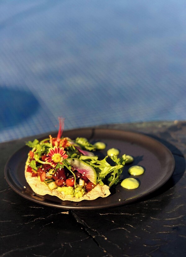 Un plato con un alimento, posiblemente un taco, sobre una superficie oscura y un fondo desenfocado.